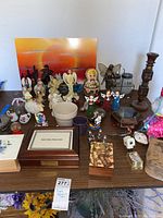 Wide view showing a variety of angel and fairy figurines along with wooden decorative boxes, candlesticks, and other small items arranged on a table.