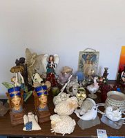 Photo showing a variety of figurines including Egyptian busts, sheep, fairies, bird figurines and an angel plaque.