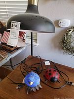 Black adjustable floor lamp with blue bird and ladybug night lights on wooden table.