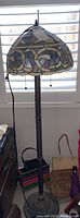 Full view of Tiffany style floor lamp near window showing stained glass shade and metal stand
