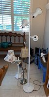 Photo showing three lamps: white floor lamp with two lights, silver metal table lamp, and beige table lamp with floral shade