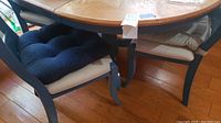Photo showing two chairs with dark wood frames and cushions, one navy blue and one beige, placed under the round oak dining table.