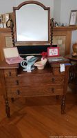 Front view of oak vanity showing four drawers, spindle legs, and attached arched mirror. Various non-sale items on vanity surface.