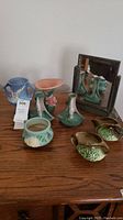 Photo showing the full lot including Roseville pottery items and a vintage mirror on a wooden surface.