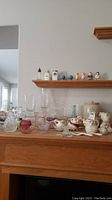 Overview of multiple vintage glass and ceramic items on wooden furniture including creamers, bowls, candle holders, and other decorative pieces.
