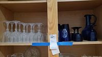 Shelf displaying clear wine glasses and dark textured decanters.