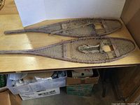 Pair of wooden snowshoes on a wooden surface showing full length and shape.