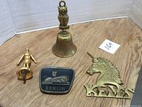 Collection of four brass items including hand bell with owl handle, small figurine, Berlin souvenir plaque and decorative unicorn figure.