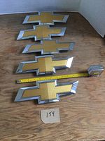Five Chevrolet bowtie emblems laid out on wooden surface, measured length is approximately 10.5 inches