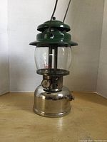 Front view of the Coleman model 236 lantern with green top and metal base on wooden surface.