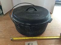 Photo of the Findlay cast iron Dutch oven from the side, showing the lid with handle and bail handle on the pot, along with a measuring tape indicating size.