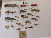 Overview of 18 fishing lures varying in size, shape and color, displayed on white background with handwritten lot number 132