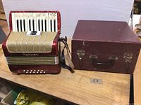 Red accordion and maroon hard case side by side on wood surface
