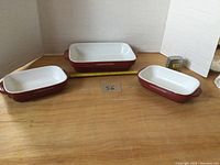 Front view of three Lagostina casseroles, showing red exterior and white interior, varying sizes, with inch tape for scale