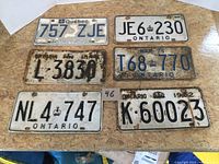 Six vintage metal license plates laid flat on a table, five Ontario and one Quebec plate, various conditions.