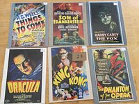 Photo showing all six reproduction movie advertising cards arranged in two rows of three, placed on a wooden surface. Titles including Things to Come, Son of Frankenstein, The Fox, Dracula, King Kong, and The Phantom of the Opera.