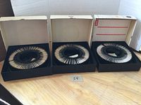 Three open boxes containing circular trays full of mounted picture slides arranged in a ring.