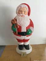 Front view of Santa Claus blow mold showing detailed facial features, red suit, green mittens, black belt, and teddy bear.