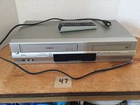 Front angled view of the Toshiba VHS and DVD combo player with power cord and remote on top.