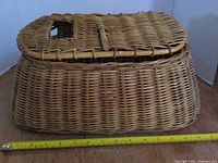 Side view of vintage woven wicker fishing creel basket showing size against measuring tape, approximately 18 inches in length.