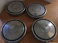 Four vintage Ford Motor Company hubcaps displayed on a wooden surface, showing front face with embossed branding.