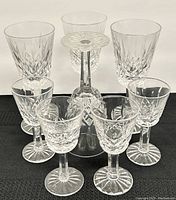 Eight Waterford crystal glasses arranged on a black surface, showing four taller aperitif glasses in back and four shorter liquor glasses in front.