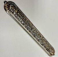 Angled view of the sterling silver mezuzah case showing embossed floral and leaf design