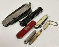 Seven assorted vintage pocket cutters and pins arranged side by side on white background, showing sizes and details.