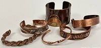 Seven vintage copper cuff bangles arranged together, showing variety in widths, designs, and finishes.