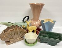 Seven vintage pottery pieces displayed including a tall pink vase, various uniquely shaped planters, and a yellow deer figurine