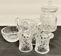 Seven Waterford crystal pieces displayed on black fabric, includes footed lidded mustard bowl, sugar bowl, creamer, and napkin rings