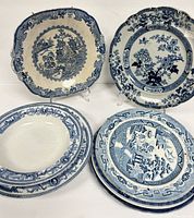 Eight blue and white antique bone china plates showing different traditional designs with visible wear and aged condition