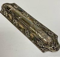 Close-up photo showing front side of the sterling silver mezuzah case with detailed repousse floral design and embossed decorations.