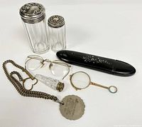 Photo showing entire lot including eyeglasses, magnifying glass, glass jars with silver lids, decorative case, and metal tag on chain