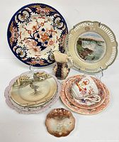 Lot of assorted antique chinaware including decorative plates, a pitcher, tea cup and saucer, photographed on white background.