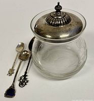 Honey jar with etched glass body and tarnished sterling silver lid with finial knob, showing crack near lid edge.