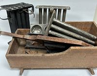 Photo of multiple metal cylindrical molds in a wooden box, showing a larger black mold and two smaller molds stacked