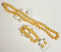 Photo of the entire jewelry set showing the necklace, bracelet, and button pearl stud earrings on white display stand.