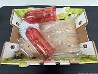 Top view showing assorted clear and red glass chimneys laid inside a cardboard box.