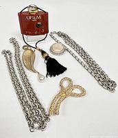 Full view of lot showing Yves Saint Laurent Opium miniature perfume bottle, chainlink necklaces, brooches including Mother of Pearl and leaf pendant with pearl and tassel.