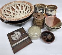 Photo shows the full set of vintage signed potteryware including the large bowl, mugs, small bowls, lidded container, stacked bowls, lattice serving bowl and decorative plate.