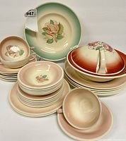 Overall view of assorted Susie Cooper porcelain dishes laid out showing different colors and floral patterns, including plates, cups, saucers, and a covered serving dish.