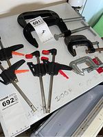 Image showing six clamps on a white surface including large black C clamps and smaller T clamps with black and orange handles.