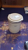 Full view of beige stoneware crock with lid on top, showing shape and general appearance.