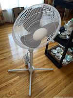 Front view of the white electric floor fan showing the three blades and circular grille on a wooden floor.