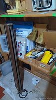 Photo of shelf with small metal lamp, air filters, cardboard boxes containing electrical sockets and outlets, flashlight, heaters, and drop cloth below