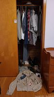 Photo of closet hanging with assortment of men's shirts, jackets, and pants, plus items laid on floor including RCAF jacket with patches and some paperwork.