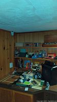 Wide view of basement corner with shelves and table holding various office supplies including paper shredder, stationery, and measuring tools.