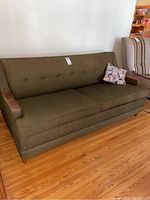Full view of retro green sofa bed with wooden armrests and cat throw pillow on the right side of the sofa.
