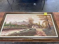 Full view of the 53x30 inch countryside oil painting showing the rural scene with cabin, trees, and mountains, inside a carved wood frame.